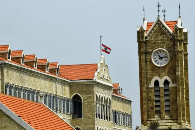 The Lebanese flag is at half-mast in Beirut above Government Palace, with a large clocktower in the background.