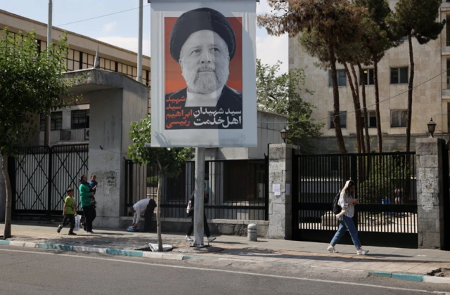 People walk near a banner with a picture of the late Iran's President Ebrahim Raisi on a street in Tehran