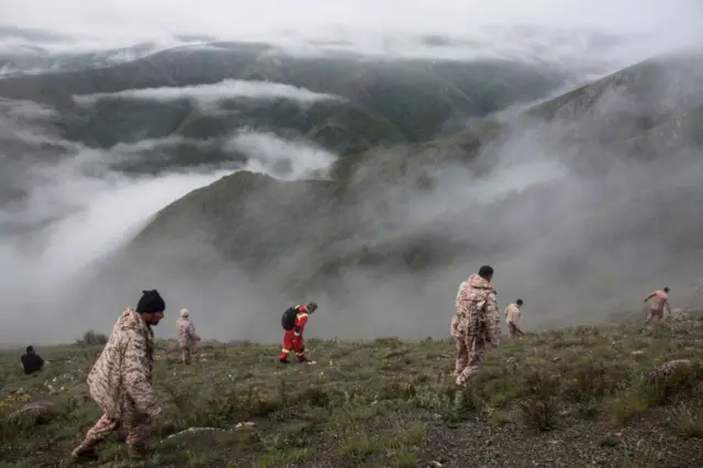 Several rescue workers search for wreckage on mountainous terrain and amid fog in Varzaqan, Iran.