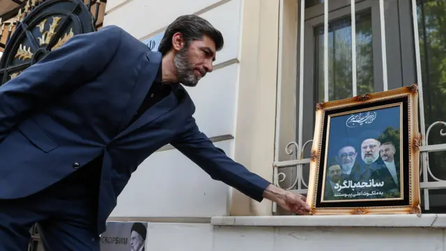 Man places hand on the frame of a tribute with a picture of four of the men killed in the helicopter crash, including President Raisi