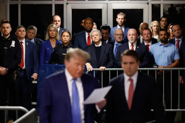 Supporters, family, and court officers watch as former U.S. President Donald Trump (front L) speaks to members of the media before entering the courtroom