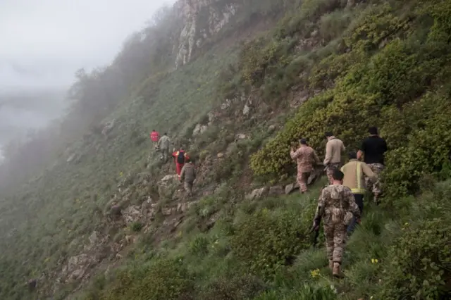 Several rescue workers walk along a mountain slope in Varzaqan, Iran.