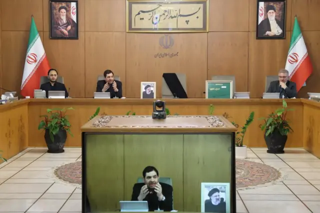 New interim Iranian President Mohammad Mokhber speaking to a cabinet meeting in Tehran. He is seated at the head of a U-shaped table with a video screen showing his address in the middle of the room.