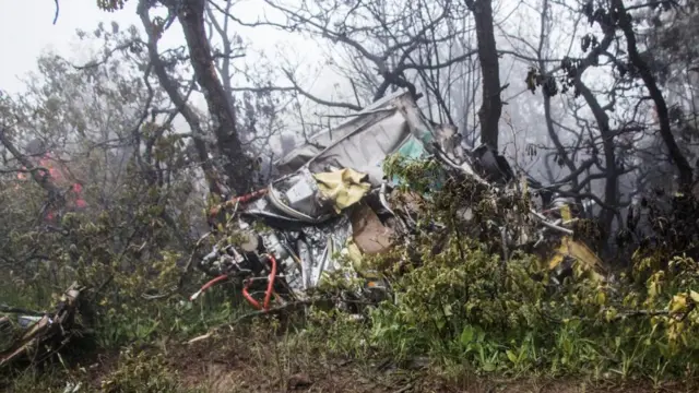 The crash site of the Iranian president's helicopter is shown on the ground, crumpled between two trees in a foggy forest area.