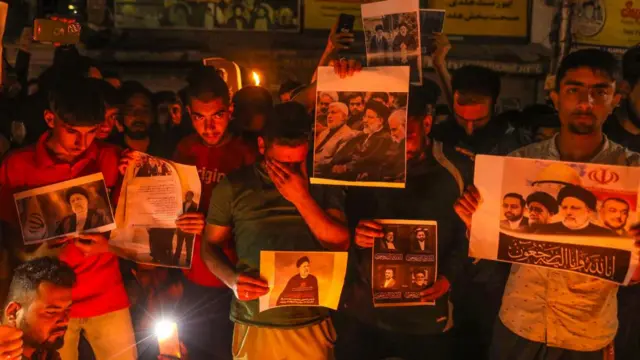 Lit by candlelight, a group of Iranian men hold photos of the deceased, their faces sombre