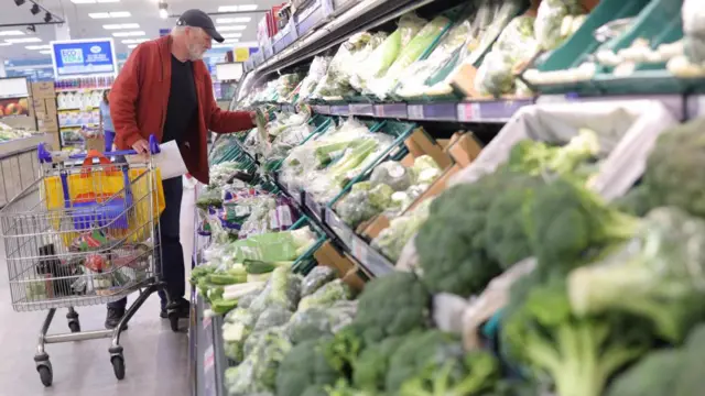 A man in a grocery store aisle examine the price of vegetables.