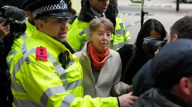 Police officer helping move a photographer in front of Paula Vennells