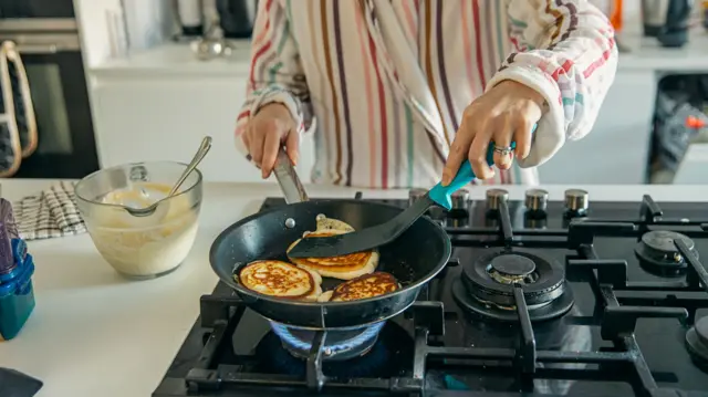 A woman cooks pancakes on a gas element