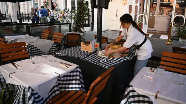 A waiter gathers plates to clear the table in an empty restaurant.