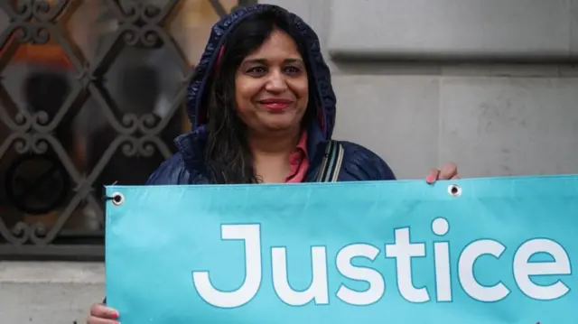 Seema Misra outside the inquiry, holding a sign which says "Justice"