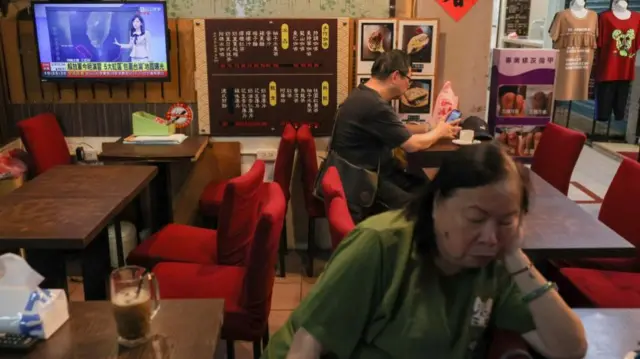 People sit in a Taiwan cafe as a news broadcast shows China's drills around island