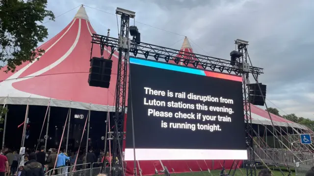 A sign on a big screen on the Big Weekend field saying There is rail disruption from Luton stations this evening. Please check if your train is running tonight.