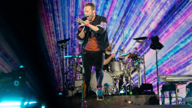 Coldplay performing on stage in front of a rainbow of lights behind them