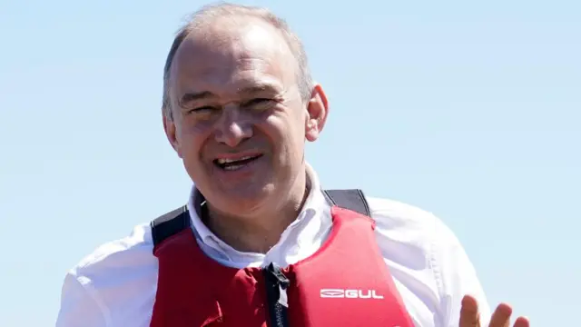 Ed Davey stands in close up dressed in a life vest.