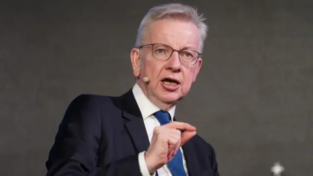 Michael Gove stands dressed in a blue suit and a blue tie.