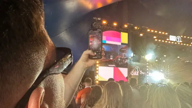 A person in the crowd holds up a phone to capture an image of the stage.