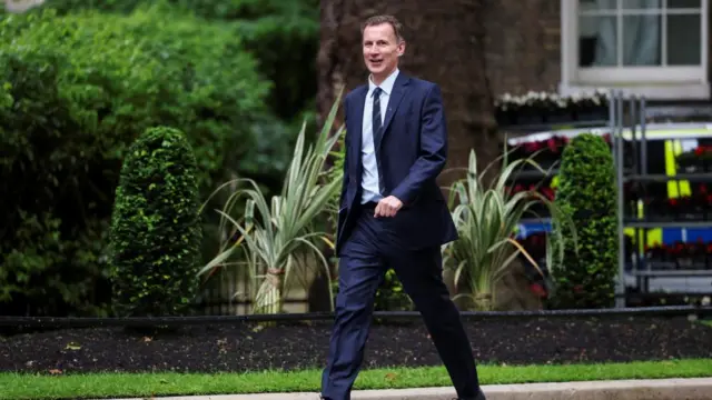 Jeremy Hunt walks outside with a folder.