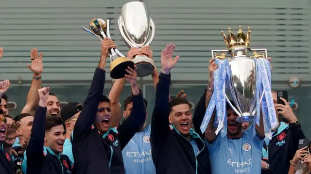 Rodri holds the Club World Cup, Kyle Walker holds the Premier League Trophy Ruben Diaz holds the Super Cup in the Manchester City victory parade