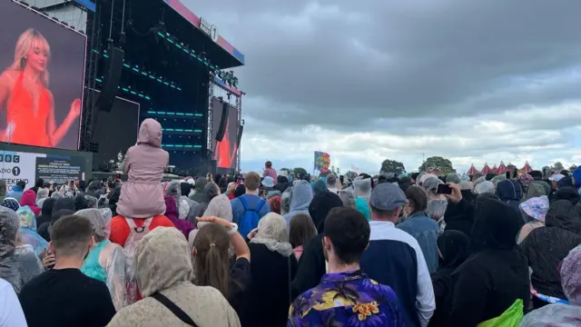 A huge crowd gathers around the stage, where Sabrina Carpenter is performing.