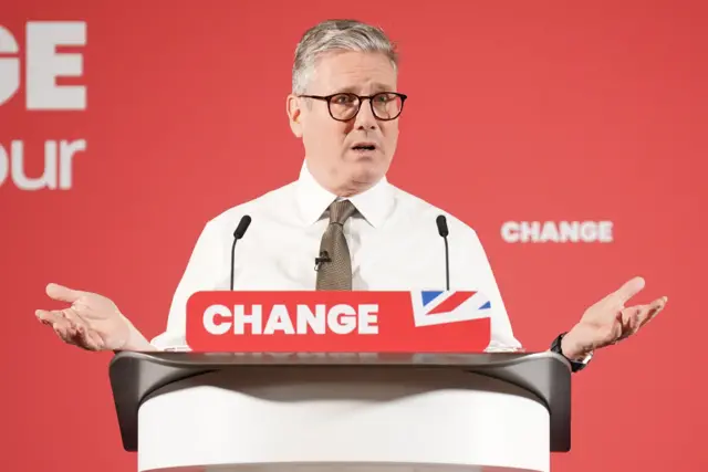 Sir Keir Starmer at a podium with two mics in front of a red Labour background