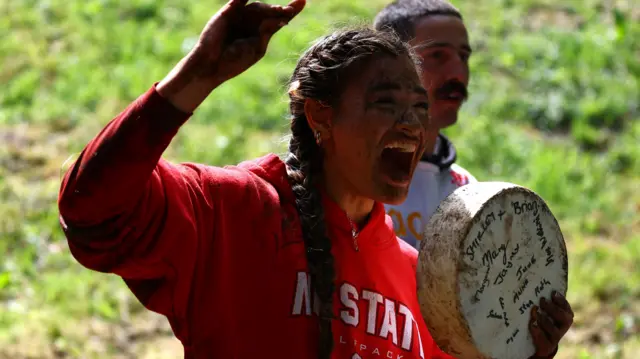 Abby Lampe is covered in mud and holding a wheel of cheese