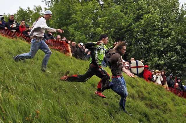 Three people chasing a wheel down a steep hill