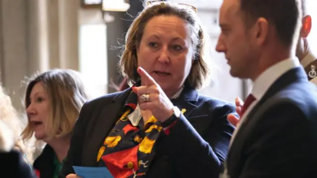 Conservative Anne-Marie Trevelyan MP surrounded by people, pointing while holding a blue card in her other hand