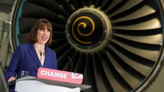 Rachel Reeves speaks at a lectern which says "change" in front of a Rolls-Royce plane engine