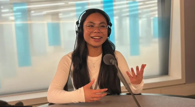 Jade Marie Carnaje wearing headphones and speaking into a microphone while gesturing with her hands