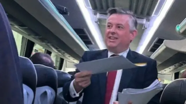 Jonathan Ashworth handing out papers in a bus