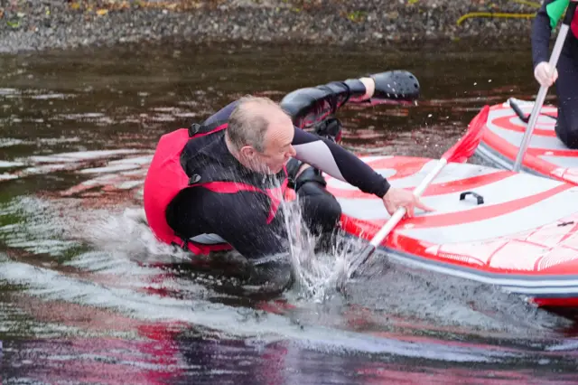 Ed Davey splashing into the water as he comes off his paddle board