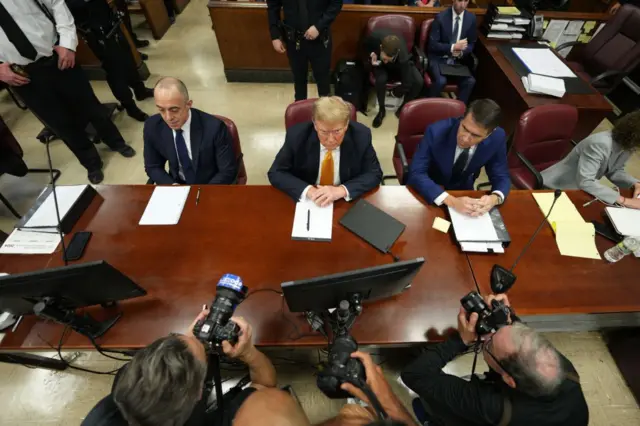 Former U.S. President Donald Trump sits in the courtroom and photographers take photos of him