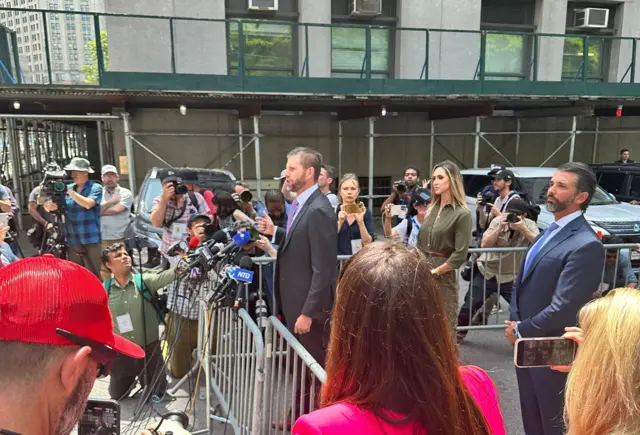 Eric Trump speaks to the media outside a New York court, while Donald Trump Jr and Lara Trump stand behind him