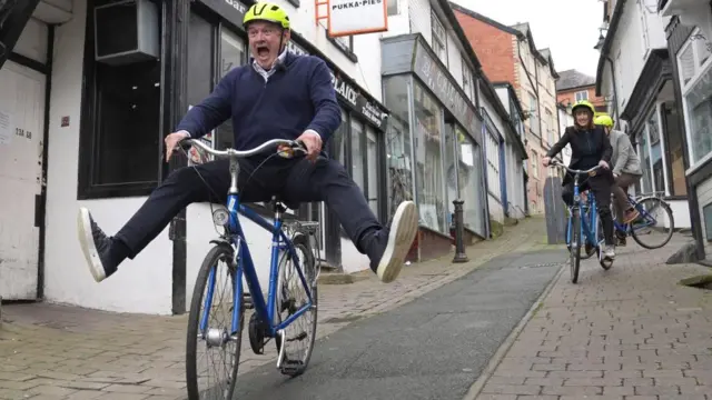 Davey rides a bike down a steep path, his legs out wide off the pedals, screaming