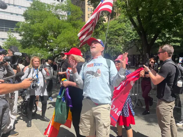 A Trump supporter stands outside court in New York, wearing a light blue shirt that says "Freedon", with a picture of a bald eagle with Trump's face pasted over the bird's head