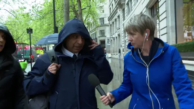 Jarnail Singh arrives at the Post Office inquiry and pulls his hood over his head, while a reporter in a blue raincoat tries to ask him questions