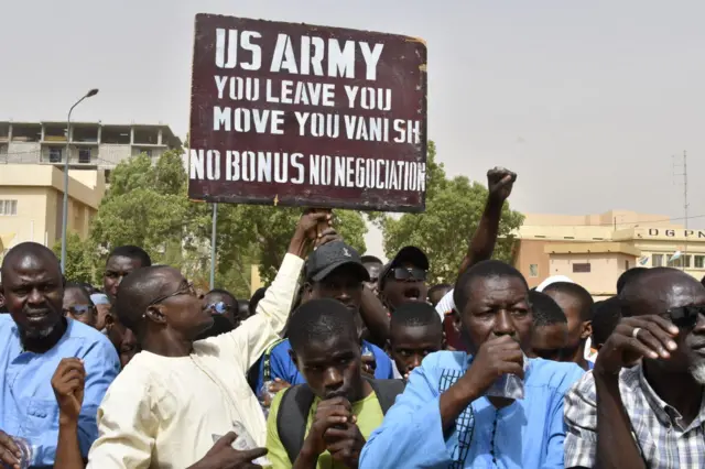 Protesters react as a man holds up a sign demanding that soldiers from the United States Army leave Niger without negotiation during a demonstration in Niamey, on April 13, 2024.