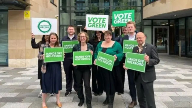 Group of Scottish Greens campaigning in Edinburgh by holding green signs saying "hands off Holyrood" and "Vote Green"