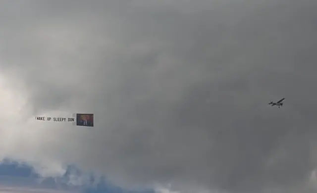 A plane tows a banner over New York which reads "wake up sleepy Don"