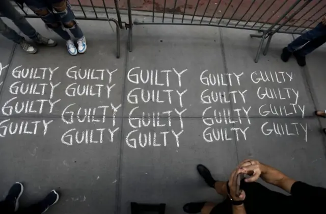 People take pictures of the words "guilty" written 34 times on the sidewalk opposite Trump Tower