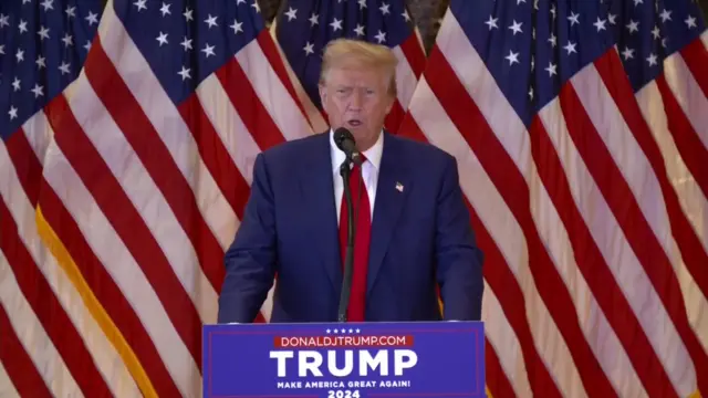 Donald Trump speaks in front of an American flag.