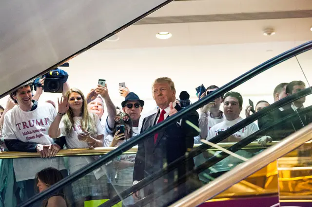 Donald Trump puts his thumb up as he rides down the escalator at Trump Tower