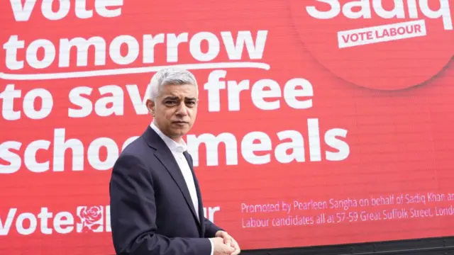 Mayor of London Sadiq Khan poses in front of a Labour sign that encourages voters to get out and vote