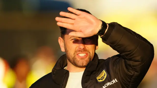 Des Buckingham shields his eyes from the unforgiving sun at Oxford United's Kassam Stadium home