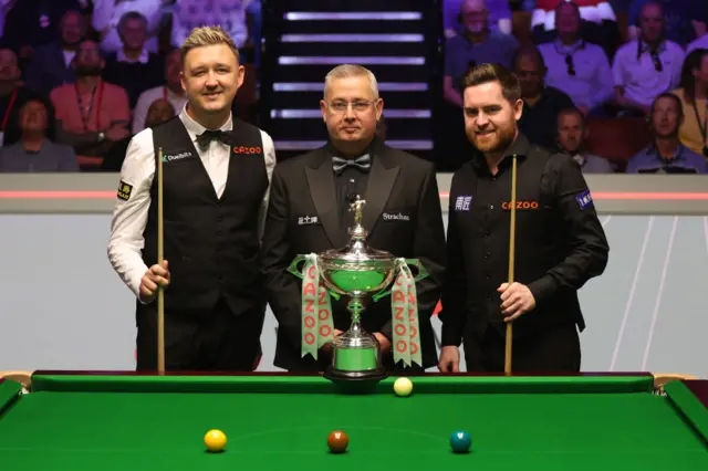 Kyren Wilson of England and Jak Jones of Wales pose for a photo with referee Paul Collier and the World Snooker Championship trophy