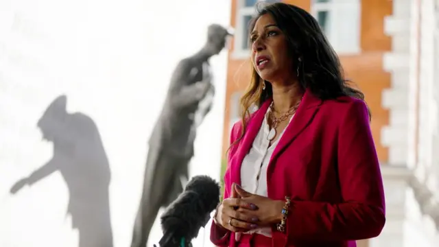 Suella Braverman speaks to media outside the BBC New Broadcasting House in a red suit.
