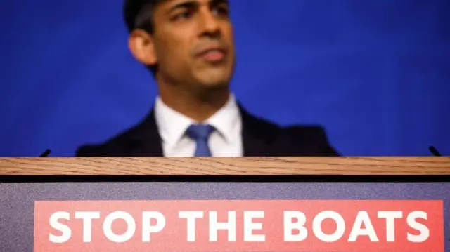 Rishi Sunak speaking about plans to send migrants to Rwanda in front of a banner that says Stop The Boats.