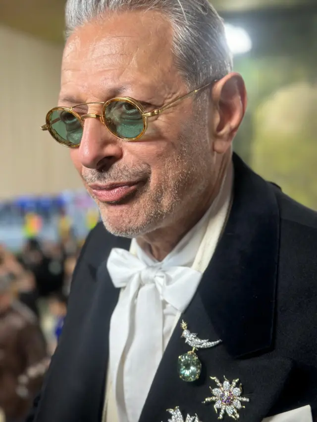 Jeff Goldblum wears a tuxedo and glasses with blue lenses