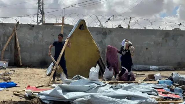 Man holds on to wooden parts of tent after it has been dismantled on the floor