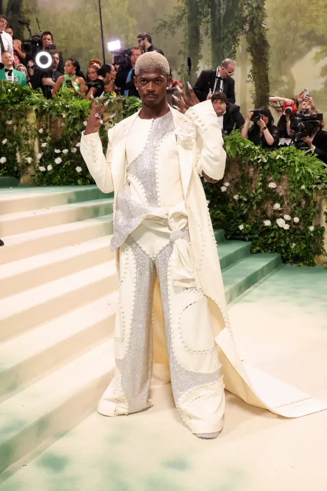 A Black man in a cream bedazzled suit with a coat that reaches the ground